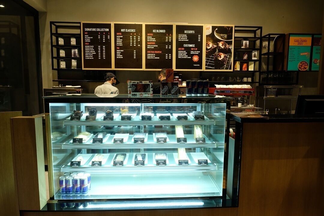 Ein Café mit einer Speisekarte, einer Vitrine mit Gebäck und einer Theke mit Barista.
