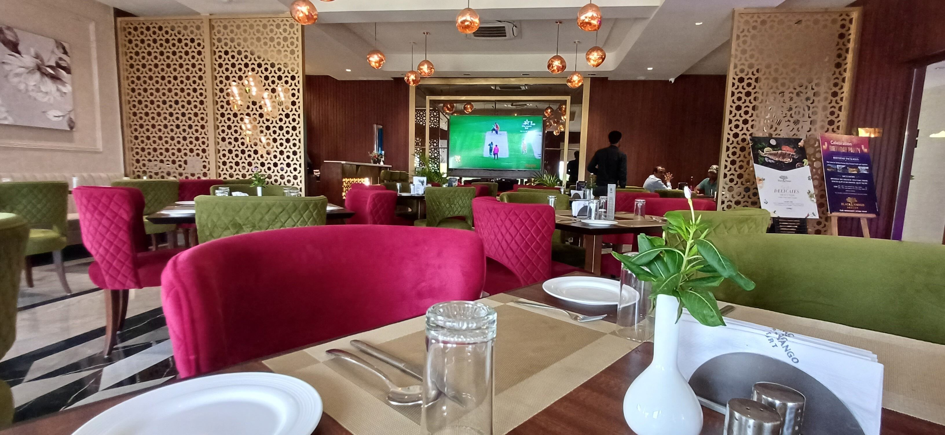 Ein Restaurant mit grün und rot gepolsterten Sitzbänken, einem Fernsehbildschirm im Hintergrund und einem Menüständer.