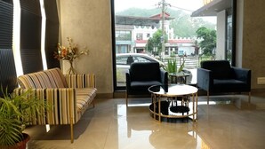 Een moderne hotelentree met een gestreept bankje, twee zwarte fauteuils, een ronde glazen salontafel en uitzicht op de straat en de bergen.