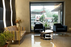 Un moderno vestíbulo de hotel con un sofá a rayas, dos sillones negros, una mesa de centro redonda de vidrio y vistas a la calle y montañas.