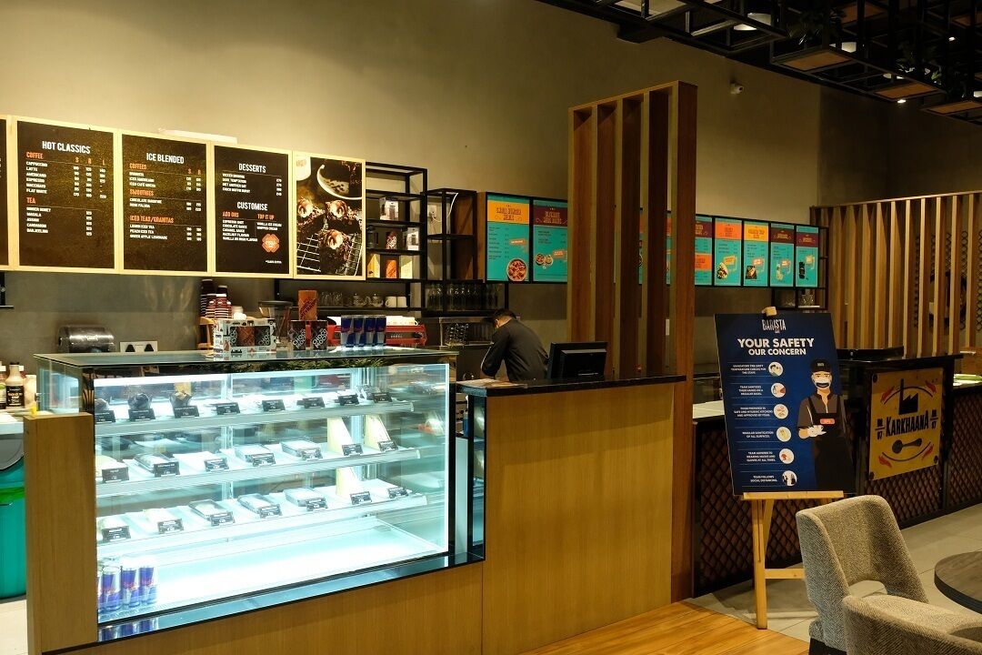 A coffee shop interior with a menu board, a display case with pastries, and a safety information poster.