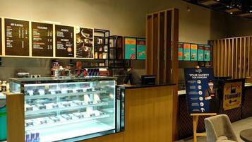 A coffee shop interior with a menu board, a display case with pastries, and a safety information poster.