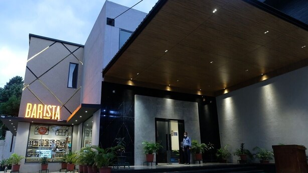 Een modern gebouw met een 'BARISTA' bord, een overdekte ingang en potplanten.