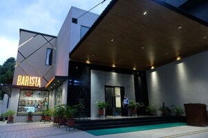 Un edificio moderno con un letrero que dice 'BARISTA', un vestíbulo cubierto y plantas en macetas.