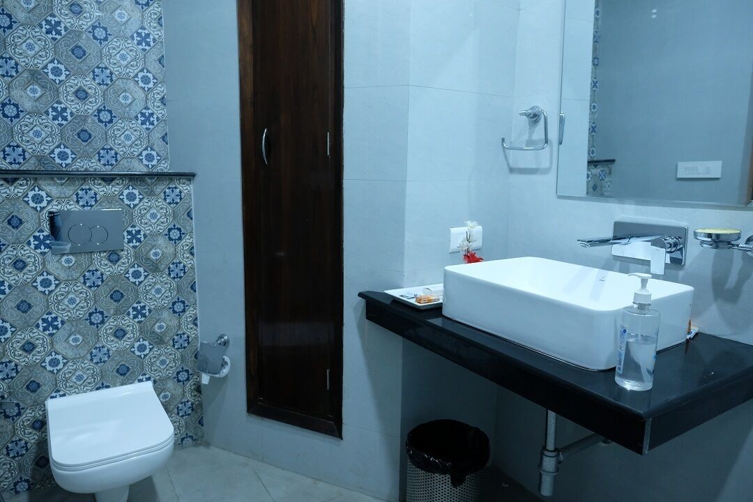 Un baño con inodoro blanco, lavamanos con espejo y baldosas estampadas en las paredes.