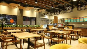 Een restaurantinterieur met houten tafels en stoelen, een toonbank met een menu, en hangende lampen.