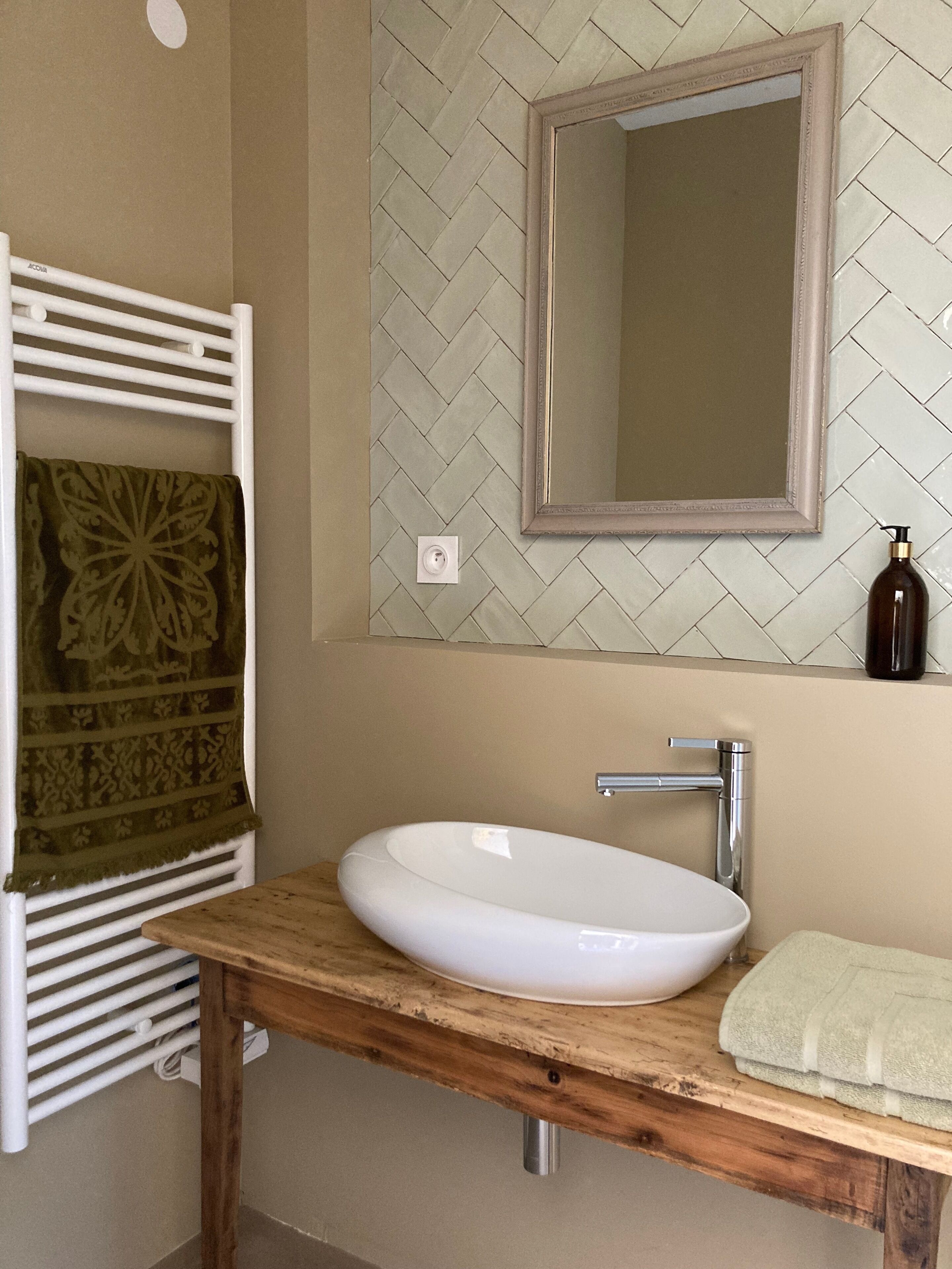 A bathroom with a white sink, a mirror, a towel rack, and a bottle of shampoo.