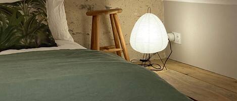 A bedroom with a bed, a wooden stool, a hanging light, and a textured wall.