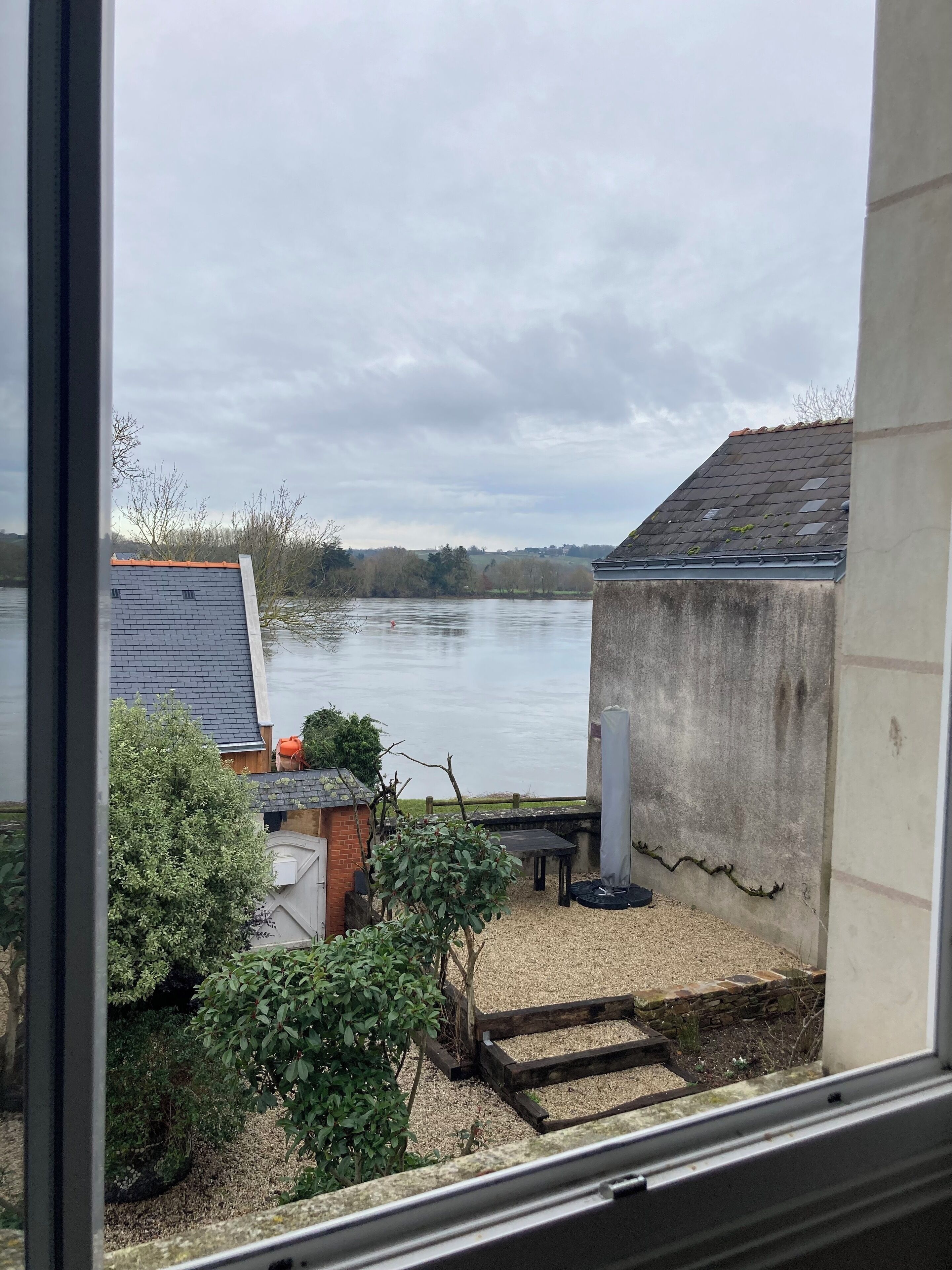 A view of a river from a window, with a building and a garden in the foreground.
