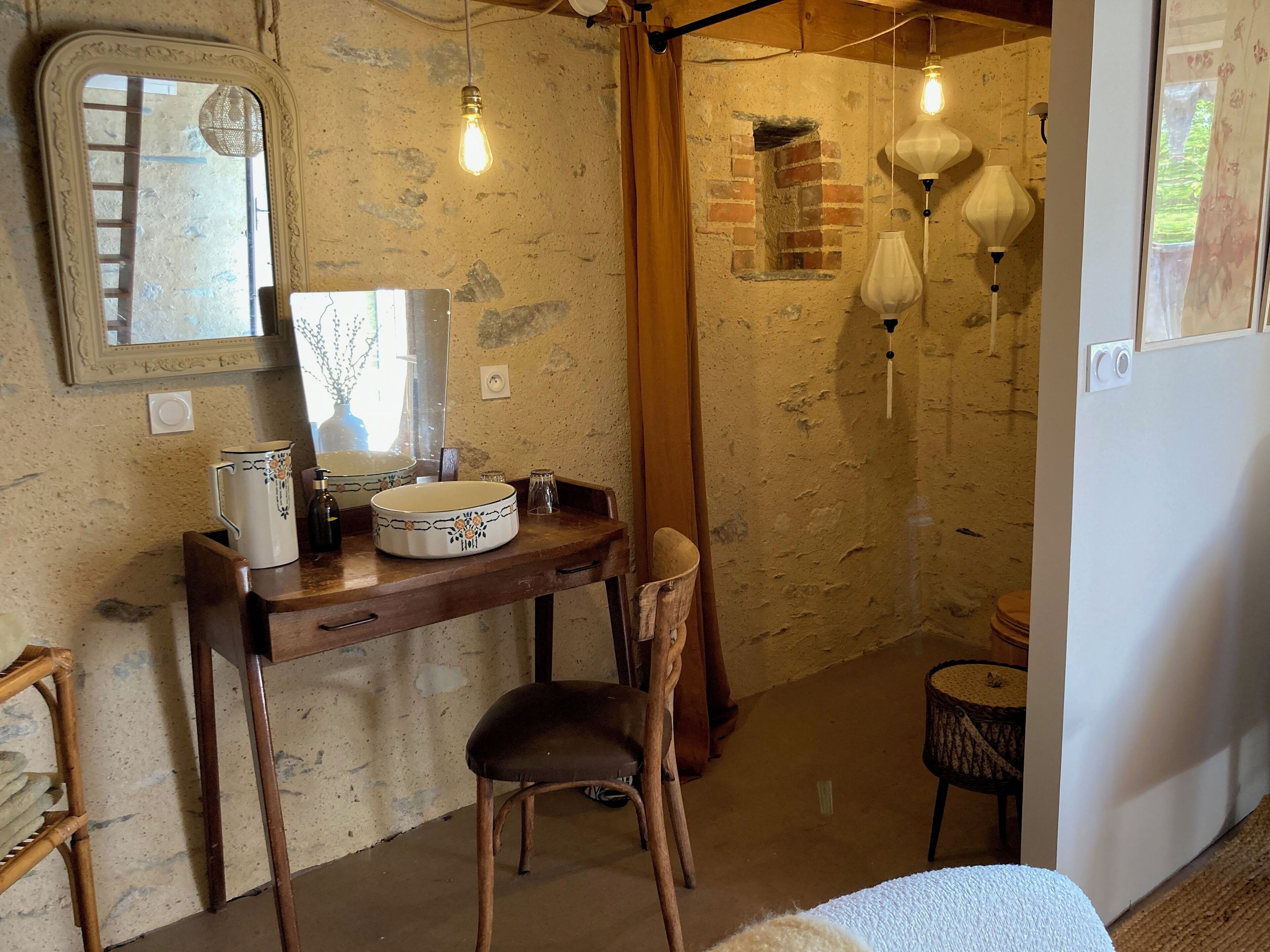 A rustic bathroom with a wooden vanity, a mirror, a sink, and a chair. There are hanging light fixtures and a small window with a view.