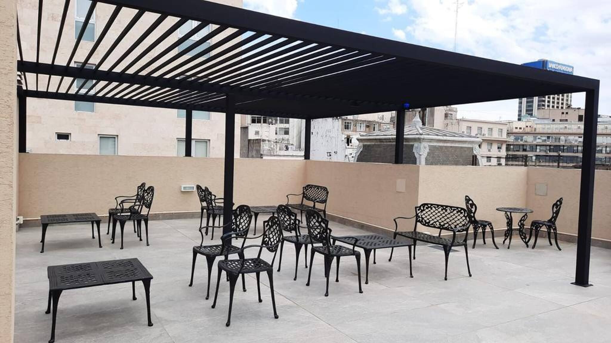 Una terraza en la azotea con mobiliario exterior, incluyendo mesas y sillas, y una pérgola.