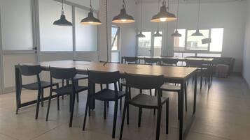 Un comedor amplio con varias mesas y sillas, ventanas grandes y lámparas colgantes.