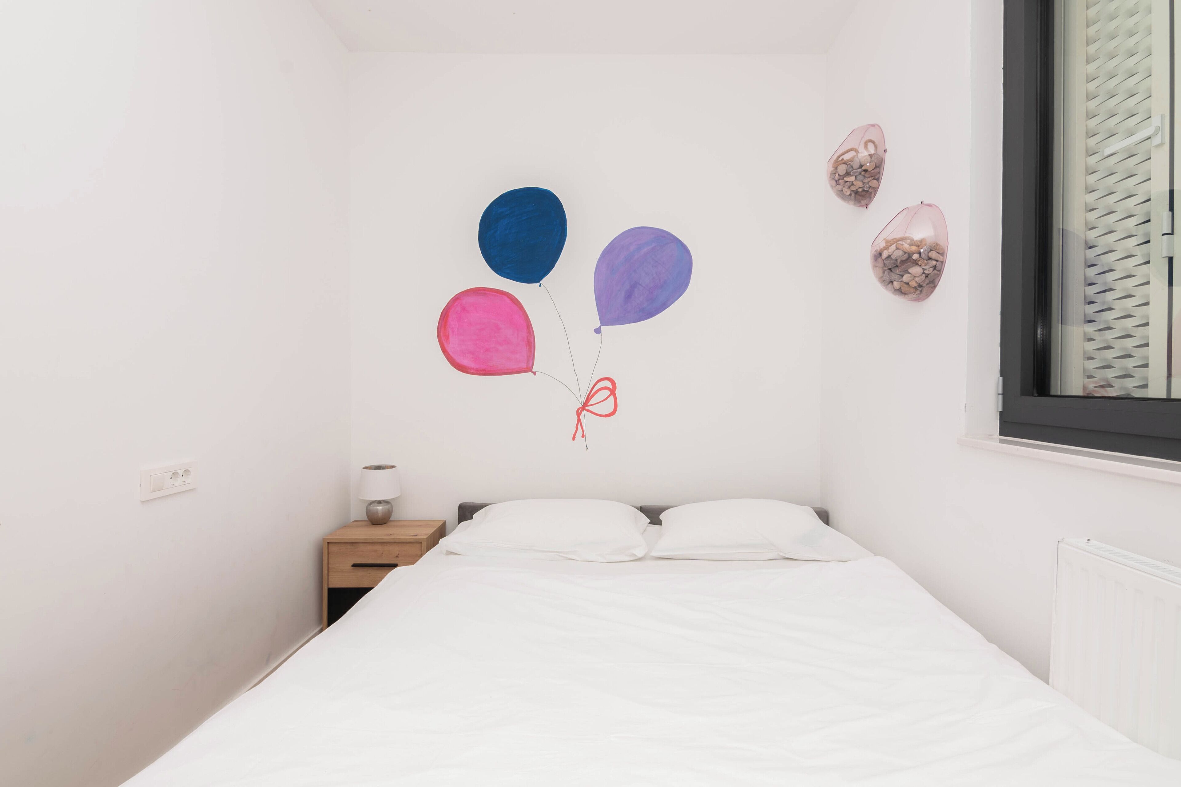 A bedroom with a bed, a nightstand, and wall decorations including balloons and a wall clock.