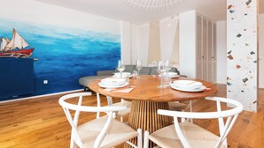 A dining area with a round wooden table set for six, white chairs, and a nautical-themed mural on the wall. - Bellavista Apartment Koper (Koper)