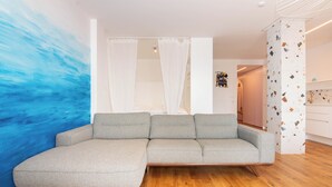 A modern living room with a grey sectional sofa, wooden flooring, and a large abstract blue painting on the wall. - Bellavista Apartment Koper (Koper)