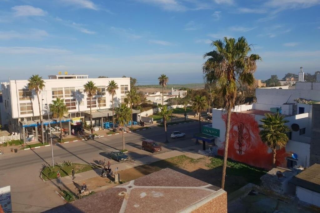 A street view with a building featuring a large mural, palm trees, and a clear sky.