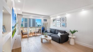 Un salon moderne avec un canapé gris, une table basse et un balcon offrant une vue sur la ville.
