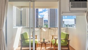 Un balcon avec vue sur de hauts immeubles, une chaise verte, une petite table et un appareil de climatisation.