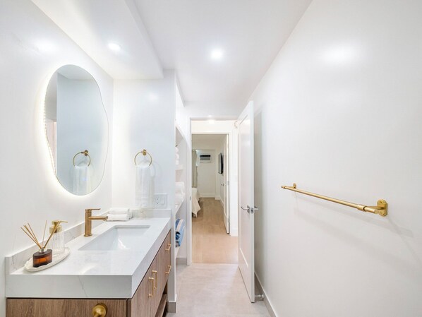 Un baño moderno con tocador blanco, detalles dorados y un espejo con iluminación integrada.