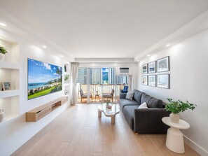 Una sala de estar moderna con un televisor de pantalla plana grande, un sofá, una mesa de centro y un balcón con vistas a la ciudad.