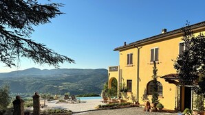 A yellow building with a gravel driveway, outdoor seating, and a view of distant hills. - Villa Tramontalba - luxury villa, infinity pool, perfect for exploring Tuscany (Toscana)
