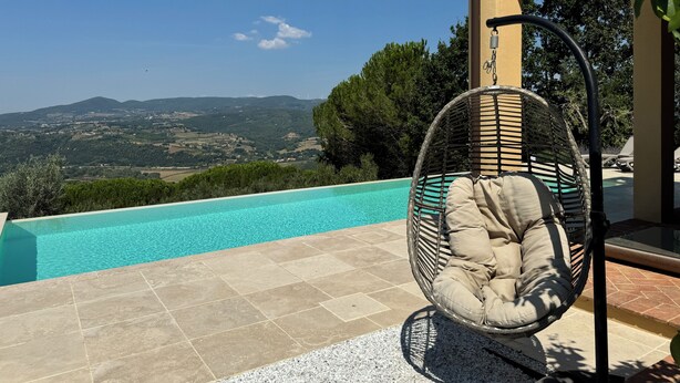 A wicker chair by a pool with a view of distant hills. - Villa Tramontalba - luxury villa, infinity pool, perfect for exploring Tuscany (Toscana)