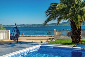 A pool area with a hanging chair, a palm tree, and a view of the sea. - Villa Morea (Sukosan)