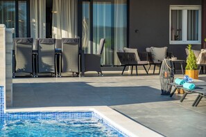 Un área junto a la piscina con sillones de descanso y una pequeña mesa con toallas.