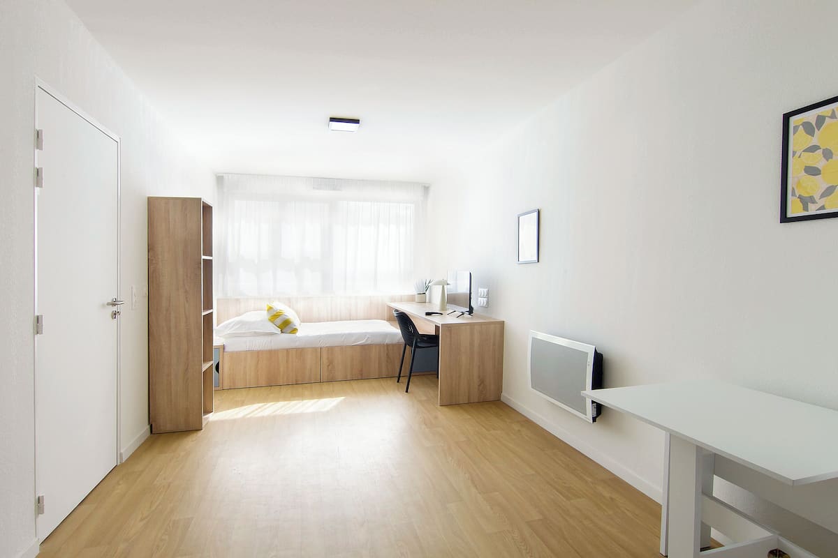 Una habitación minimalista con una cama, un escritorio y un televisor.