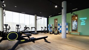 Un gimnasio con diverso equipamiento de ejercicio, amplias ventanas y un luminoso letrero de neón motivacional.