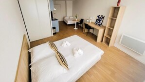 Una habitación de hotel moderna con una cama, un escritorio, una silla, un armario y un pequeño rincón de estar con una mesa y sillas.