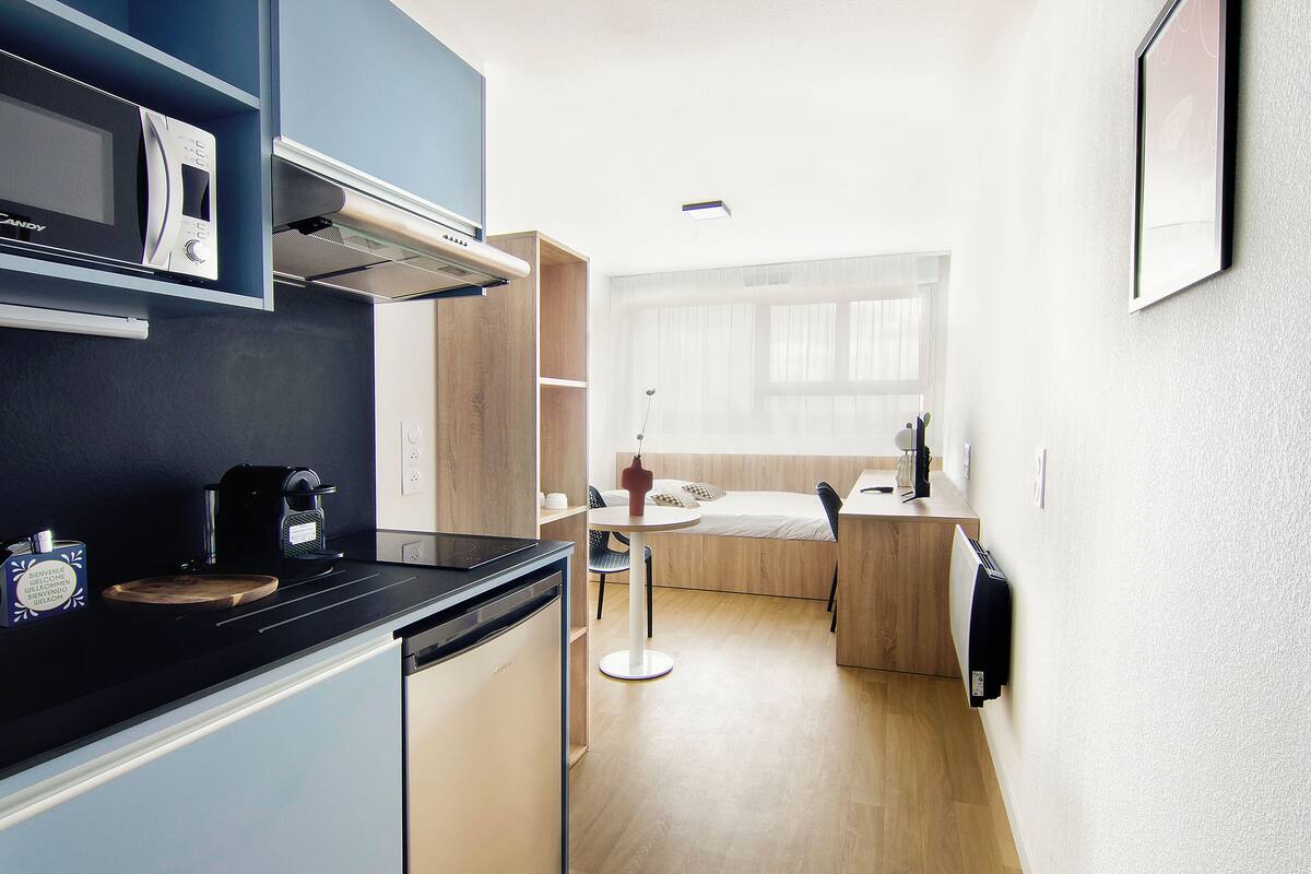 Una cocina compacta con microondas, cafetera y un pequeño comedor con mesa y sillas.
