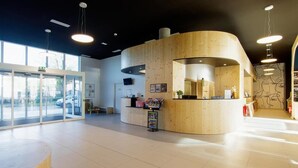 Un área de recepción moderna con un mostrador de madera, una puerta de cristal de entrada y un gran ventanal que proporciona luz natural.