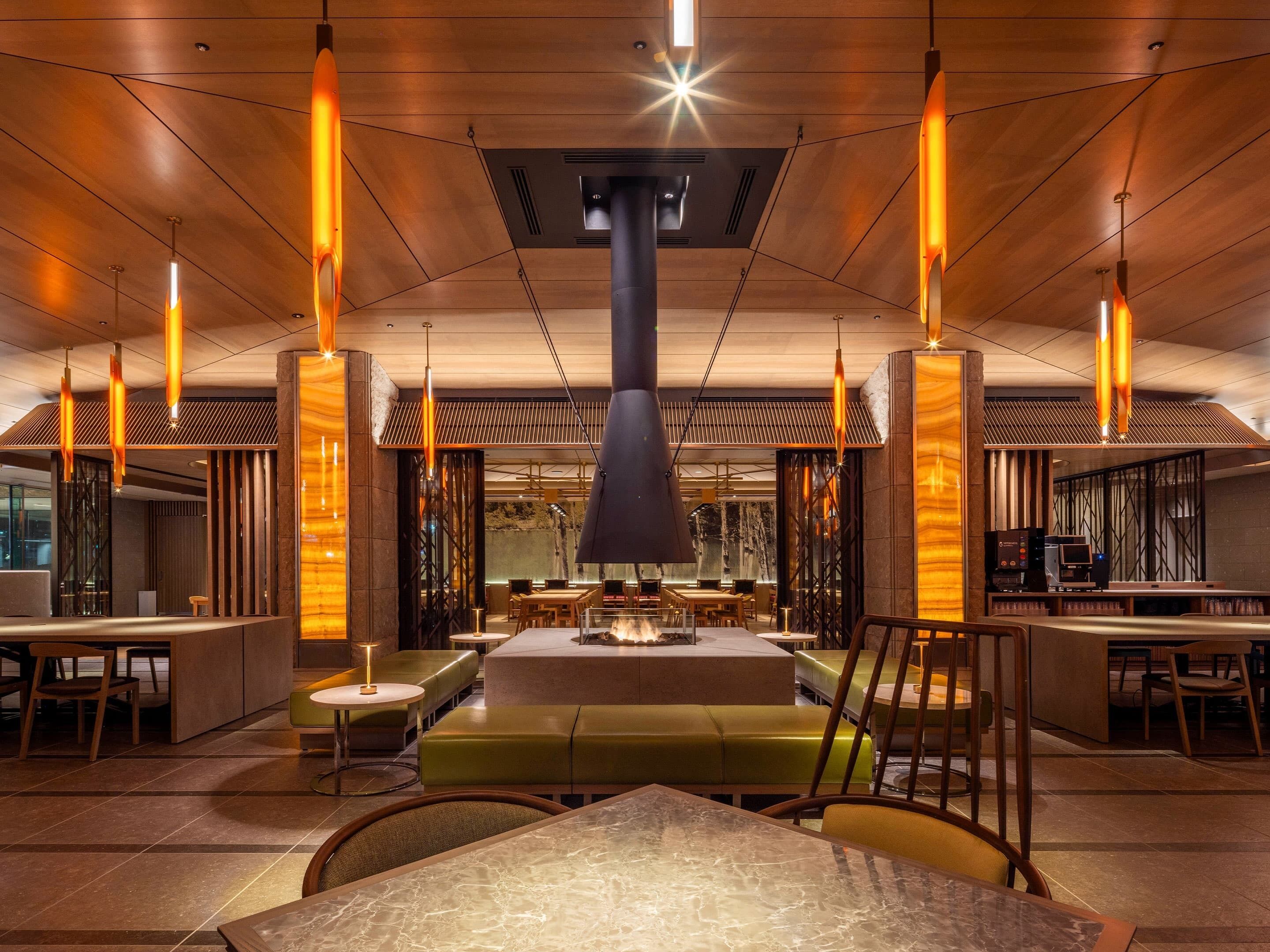 Un interior de restaurante moderno con techos altos, paneles de madera e iluminación colgante.