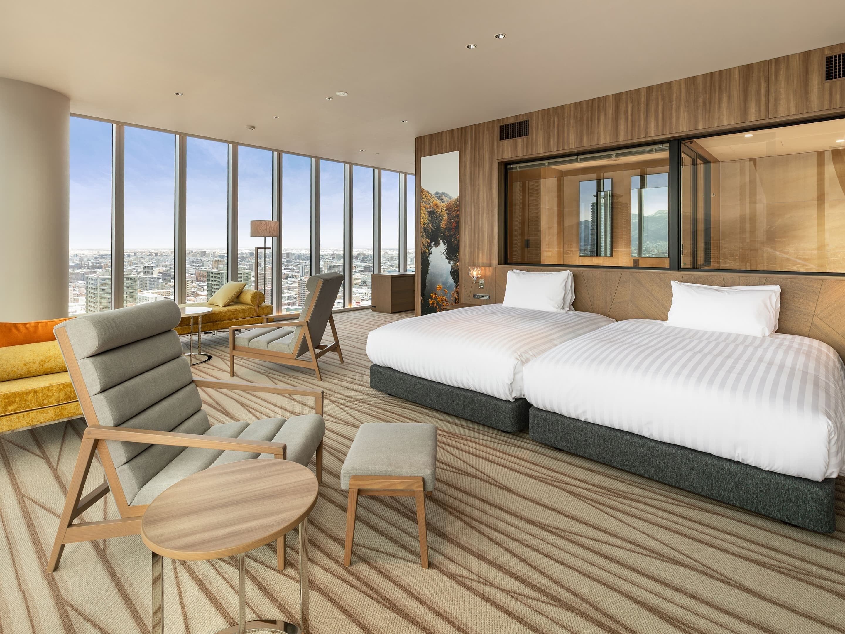 Una camera d'albergo moderna con un letto grande, un divano, una poltrona e vista sulla città.