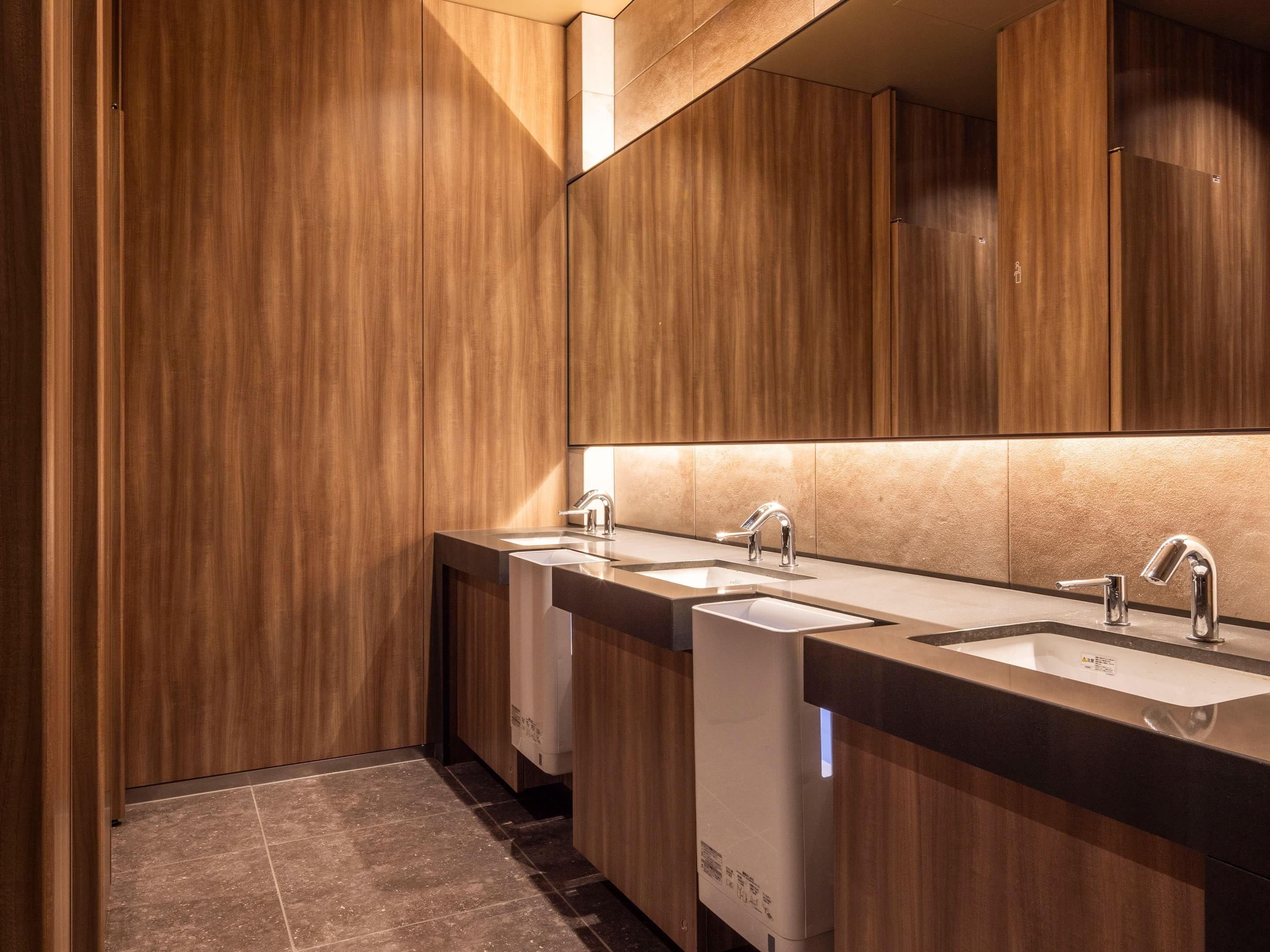 Un baño moderno con paneles de madera, tres lavamanos y un espejo grande.