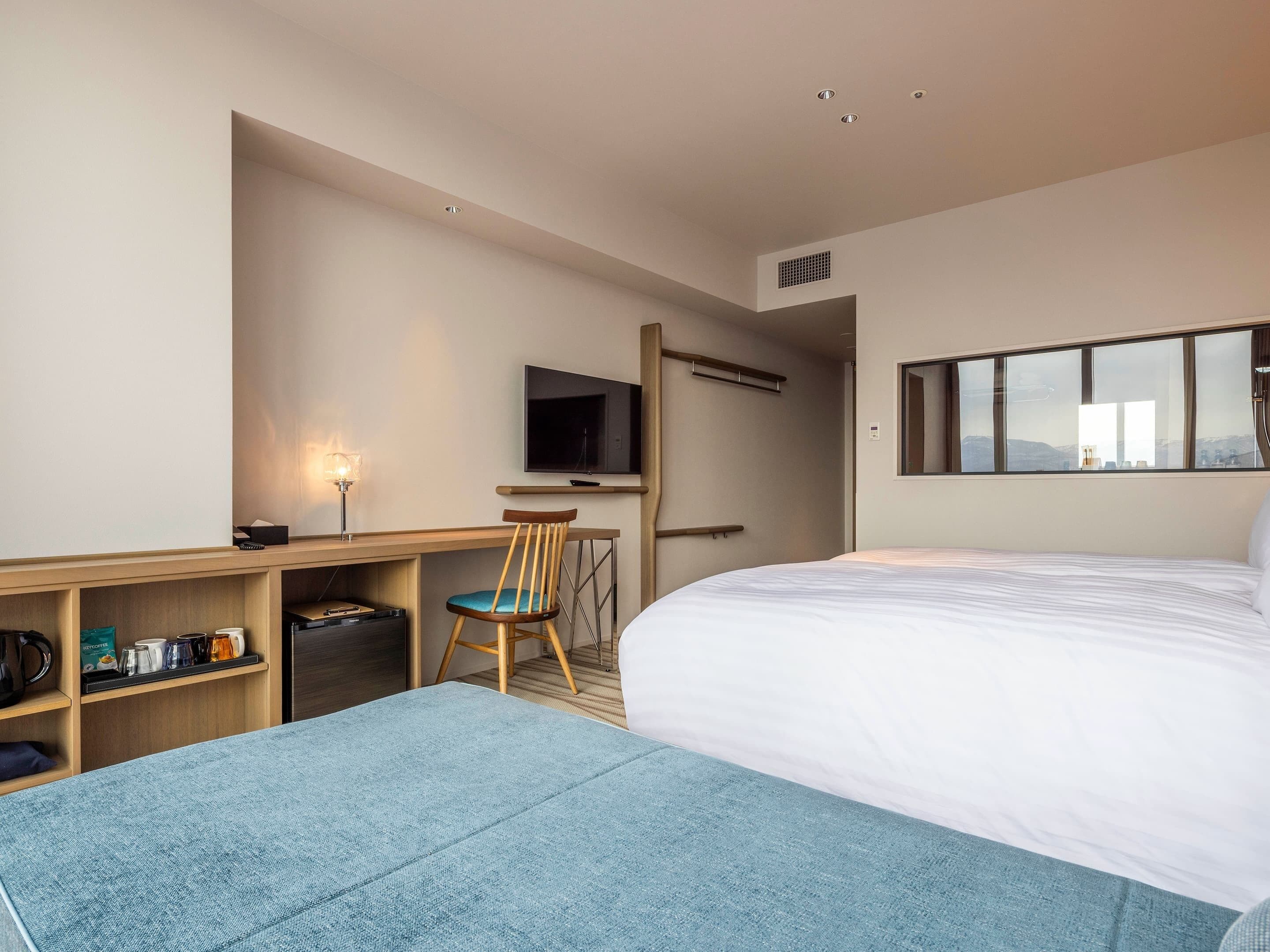 A hotel room with a bed, a desk, a chair, a TV, and a window with a view.
