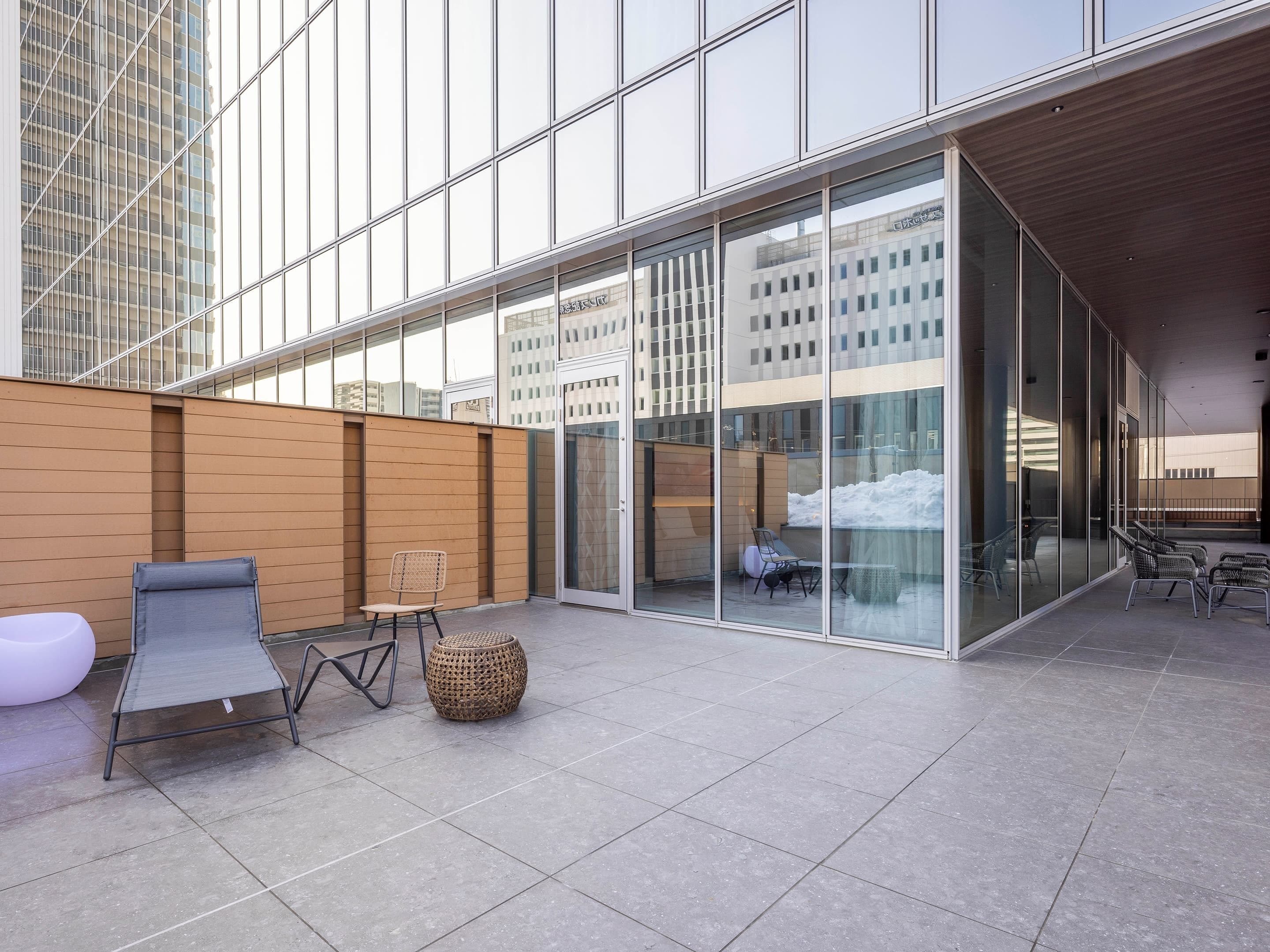 A modern outdoor terrace with glass walls, seating, and a view of the cityscape.