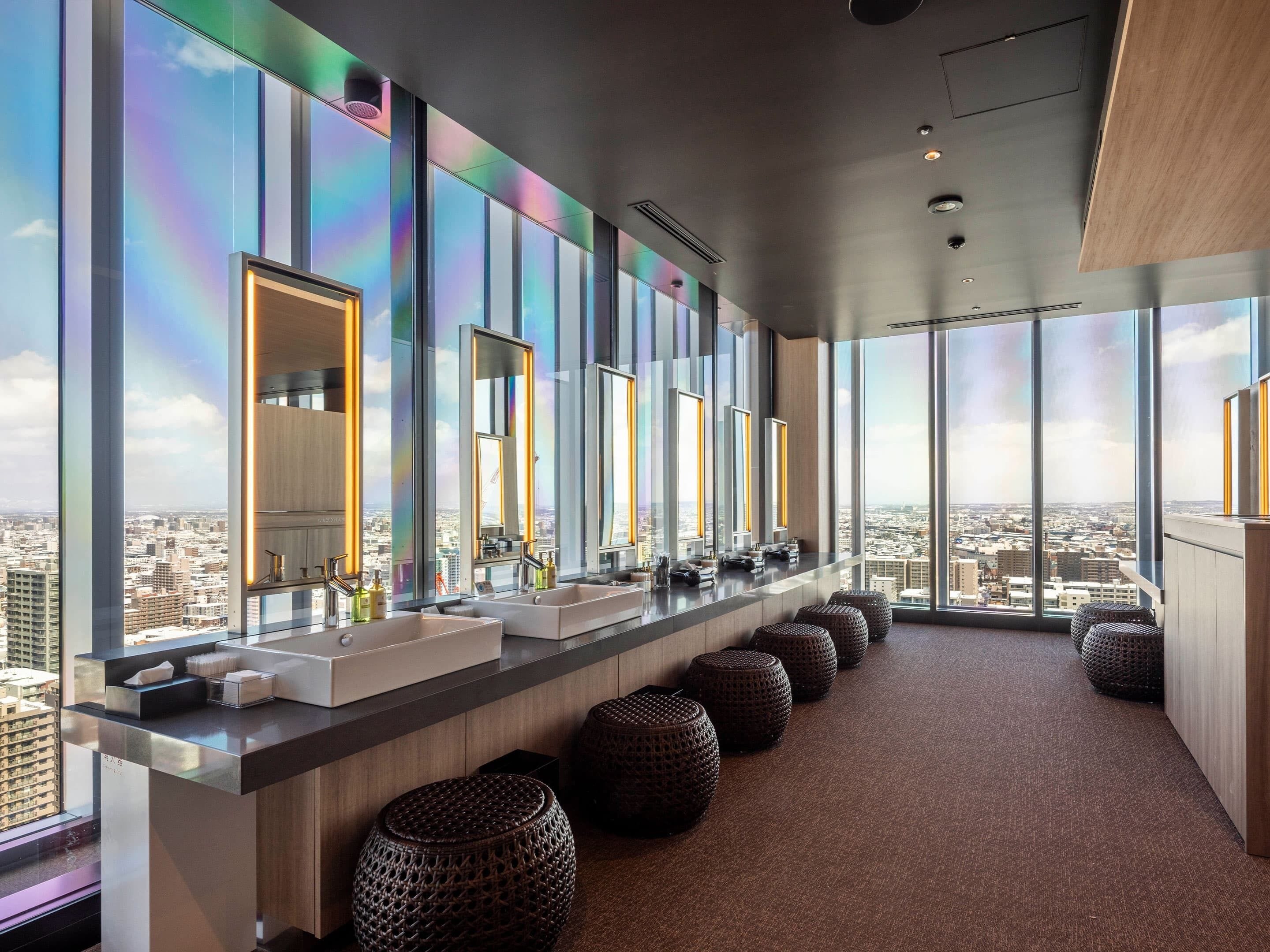 Een moderne hotelbadkamer met grote ramen, een lange wastafel met spiegels en uitzicht op de stad.