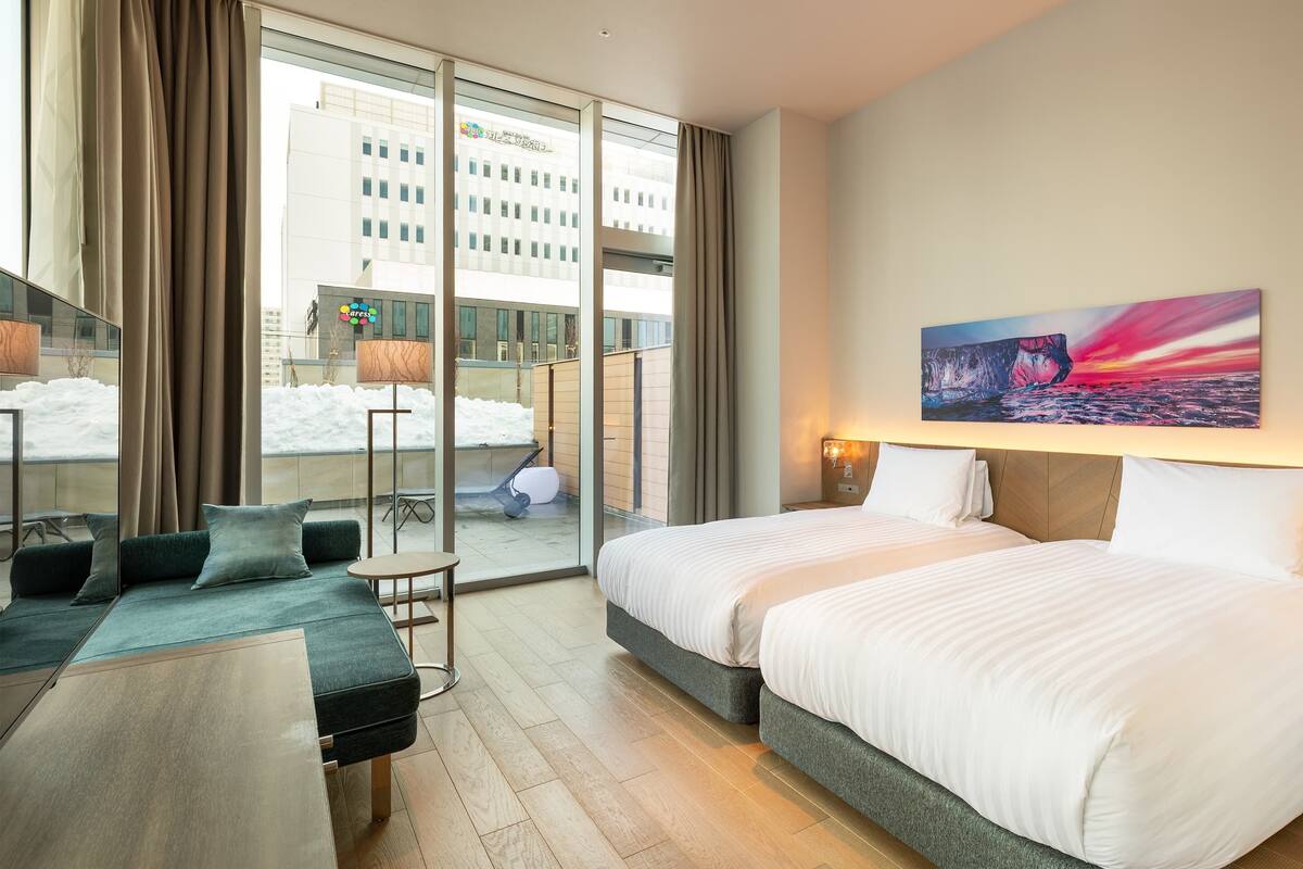 A hotel room with a large bed, a sofa, a glass wall, and a painting.