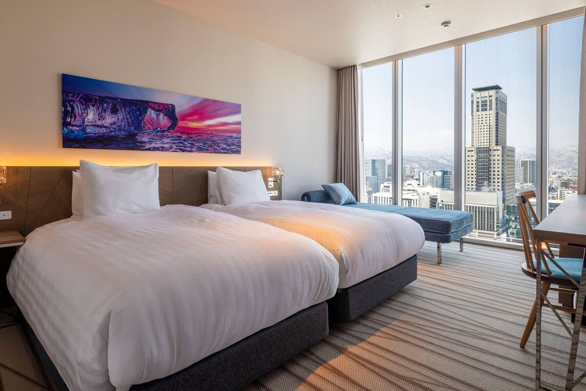 A hotel room with a large bed, a city view, and a painting on the wall.