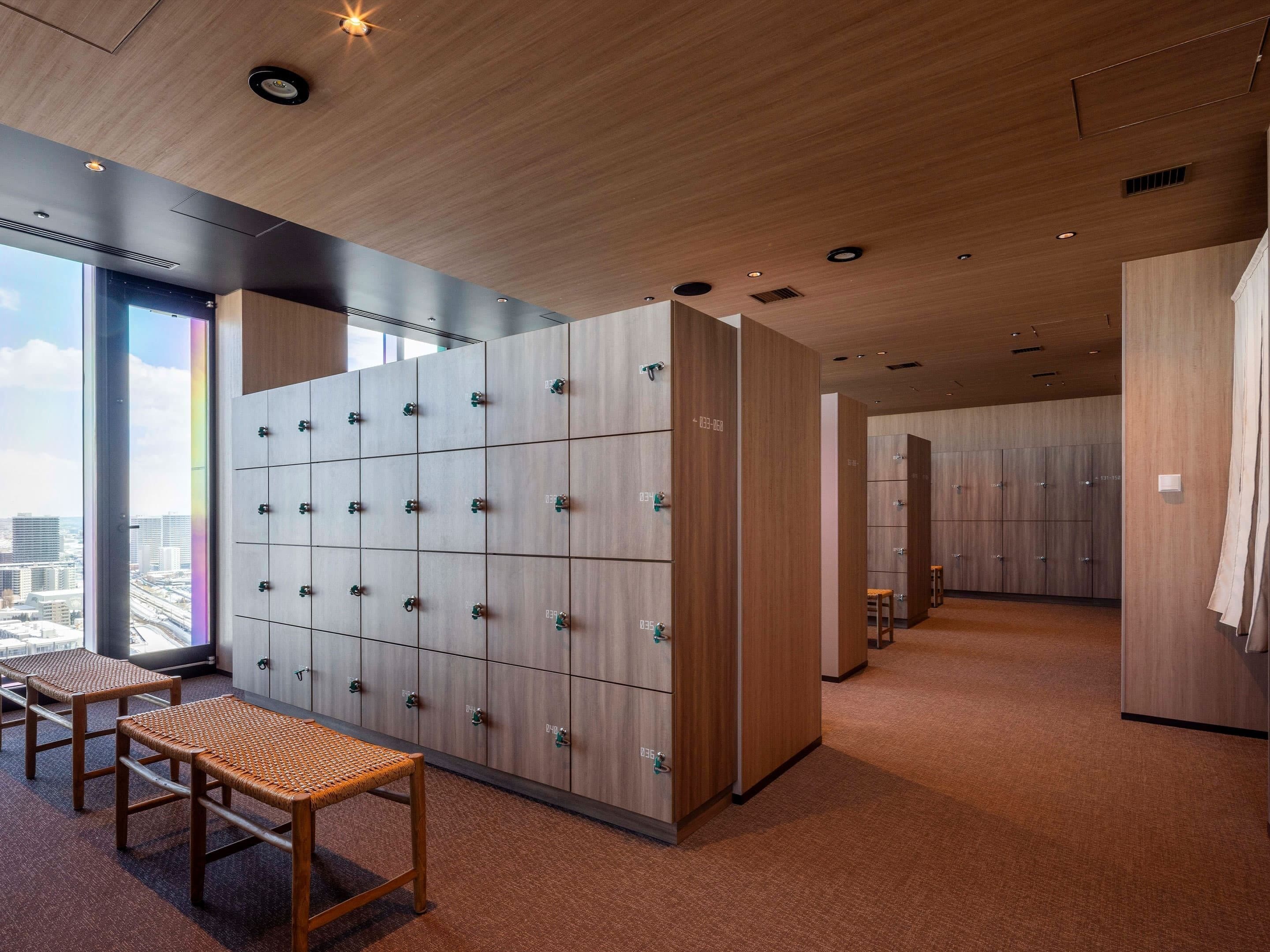 A modern hotel room with a large window, a wooden wardrobe, and a seating area.