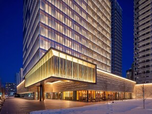 A modern hotel with a glass facade, a covered outdoor area with seating, and a snow-covered ground. - SAPPORO HOTEL by GRANBELL (Sapporo)