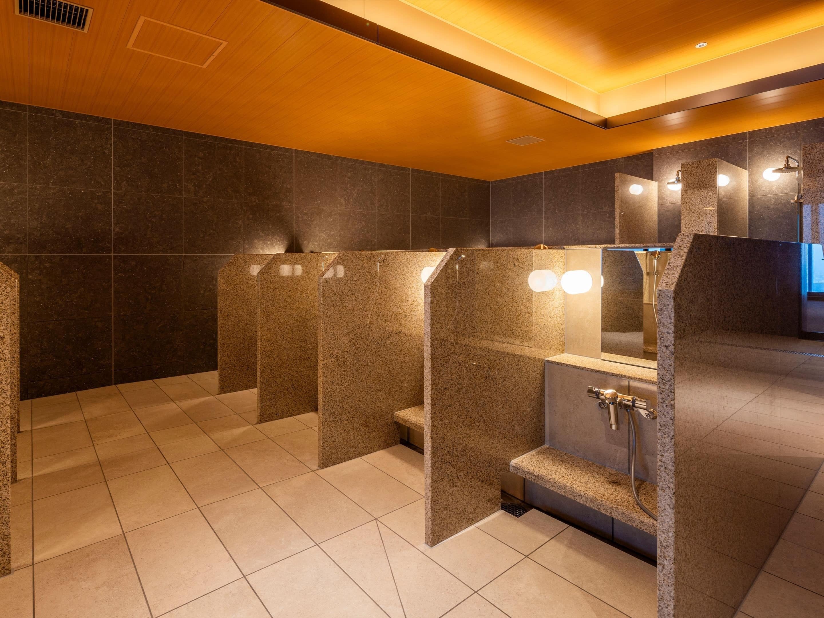 Ein modernes Badezimmer mit Granitwänden, einem zentralen Waschbecken und separaten Duschkabinen.