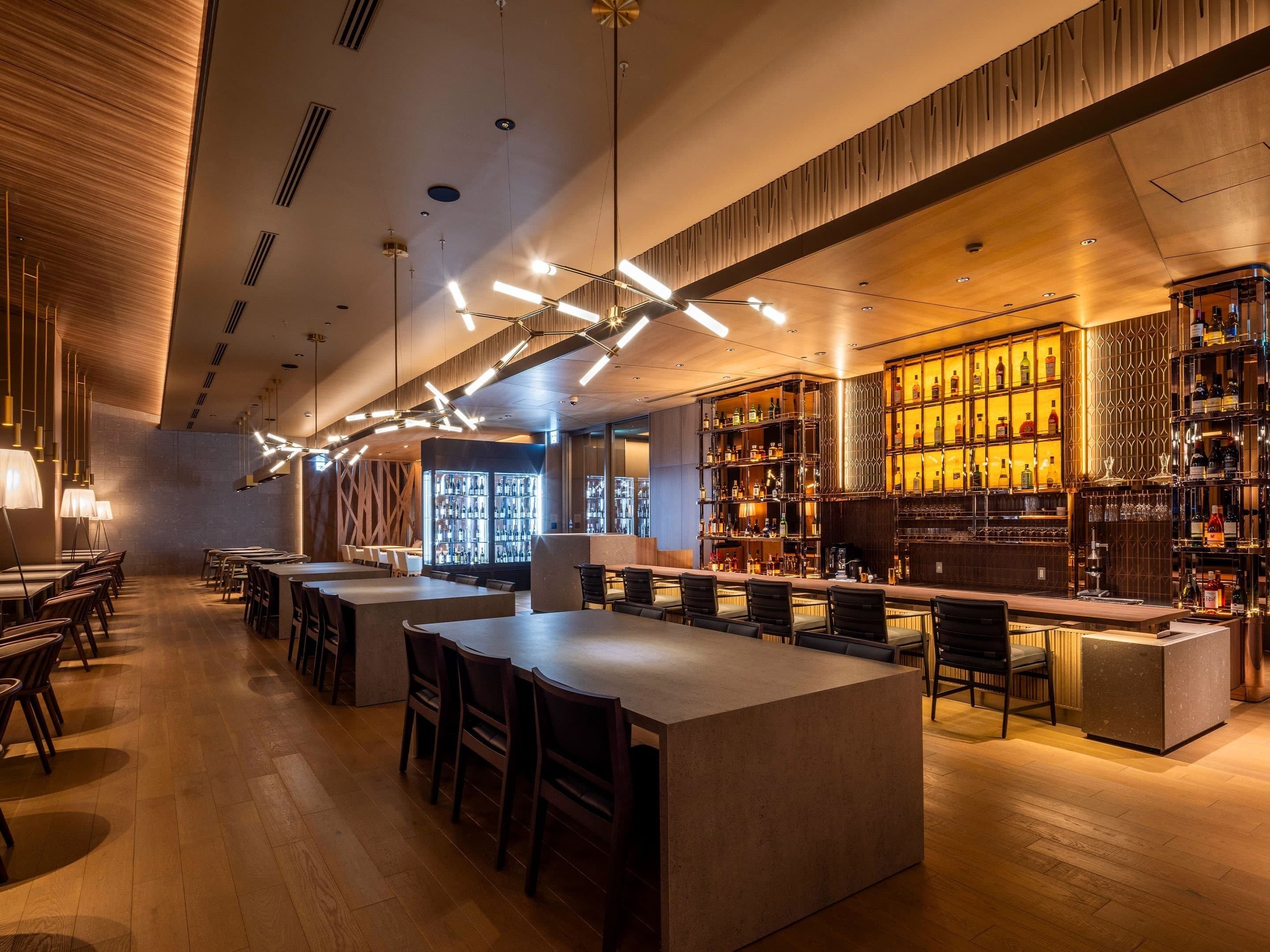 Un bar moderno con una barra larga, distintas opciones de asientos y un interior bien iluminado.