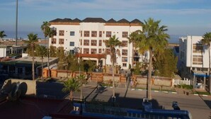 Un hotel de varios pisos con fachada blanca y detalles en marrón, con balcones y vista al mar.
