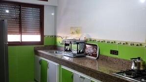 Cocina con armarios verdes, encimera de granito, cafetera y estufa.