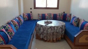 Una habitación con un sofá azul, una mesa redonda con mantel estampado y cojines decorativos.