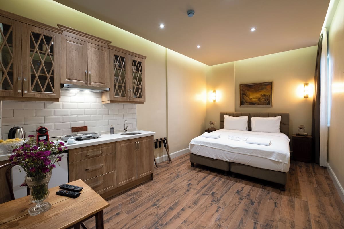 Ein kleines Hotelzimmer mit Bett, Nachttisch und einer kleinen Küchenzeile mit Holdekor und gefliestem Spritzschutz.