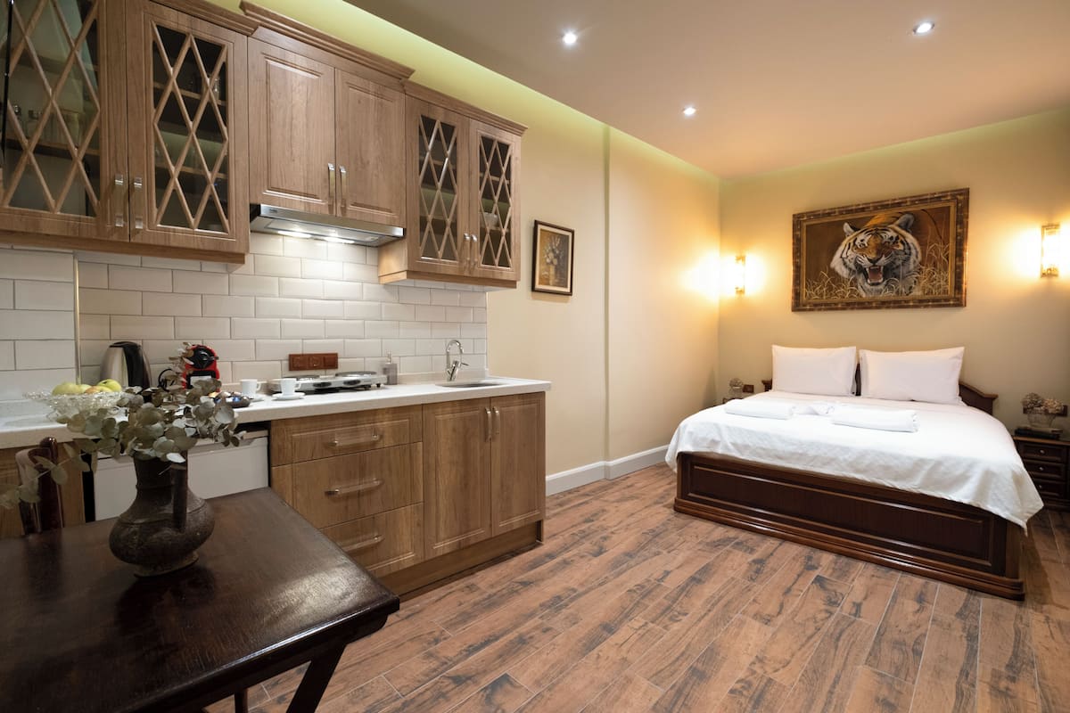 Ein Schlafzimmer mit einem großen Bett, Holzschränken, einem Esstisch mit einer Vase und einer Küchenzeile mit Herd und Schränken.